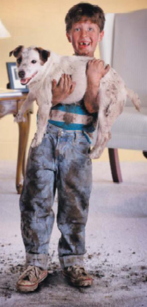A boy holding dog with mud all over carpet needs cleaning